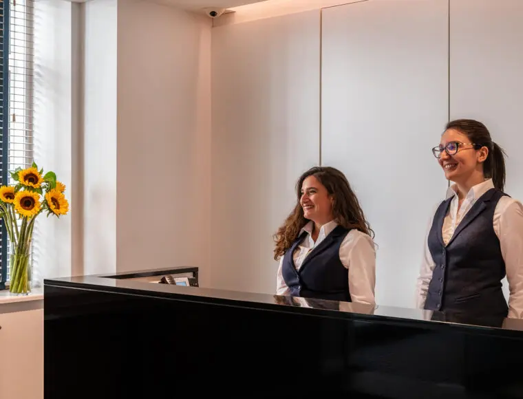 Hotel professionals stood at the reception area whilst smiling.