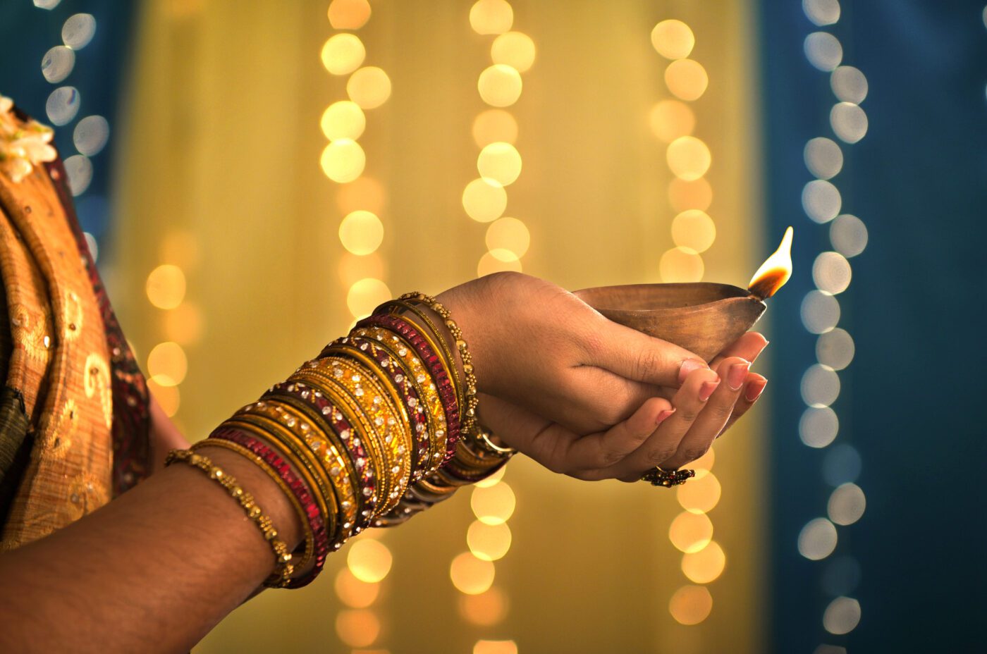 A person wearing colorful bangles holds a traditional oil lamp with a small flame during Diwali celebrations