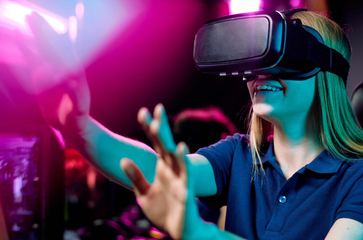 Girl using virtual reality simulator gesturing hands to bright purple light while playing video game in 3D at Game On! Exhibition at the National Museum of Scotland.